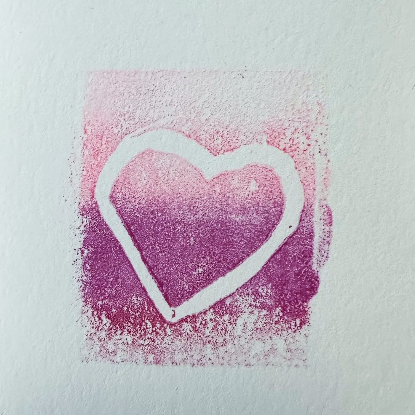 A hand-pulled magenta print with a white heart shape at its center on textured paper