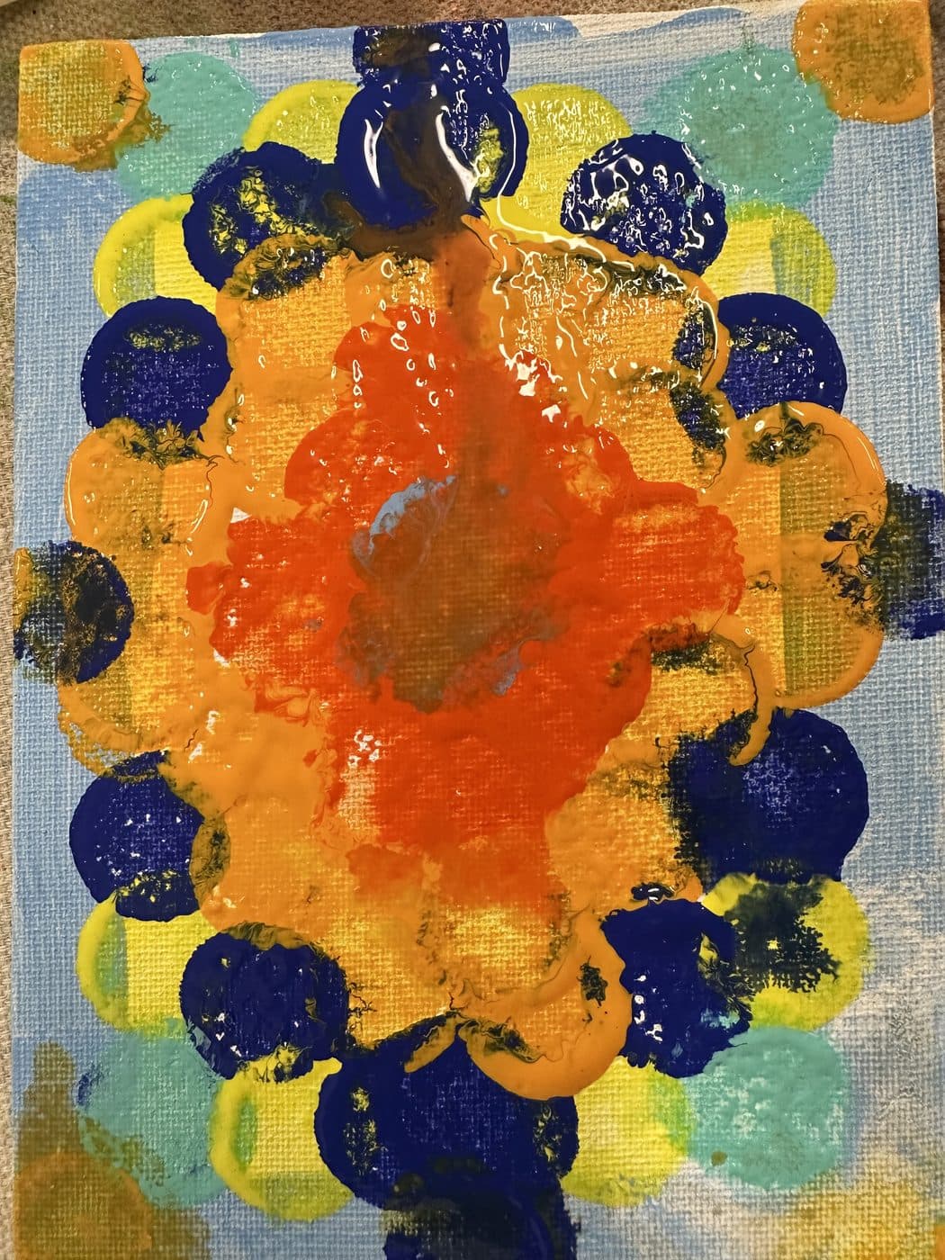 A bright painting of an orange sunburst ringed by navy and yellow sponge-printed circles